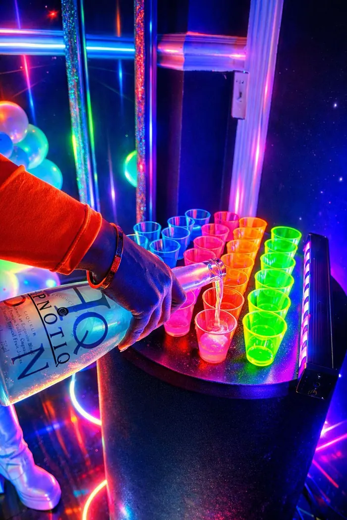 Bartender pouring a bottle into a row of neon UV shot glasses